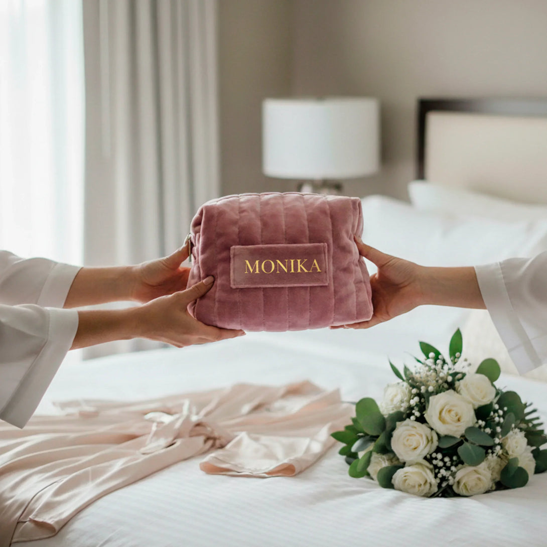 Personalized pink quilted velvet pouch with name, held by two hands over a bed with flowers